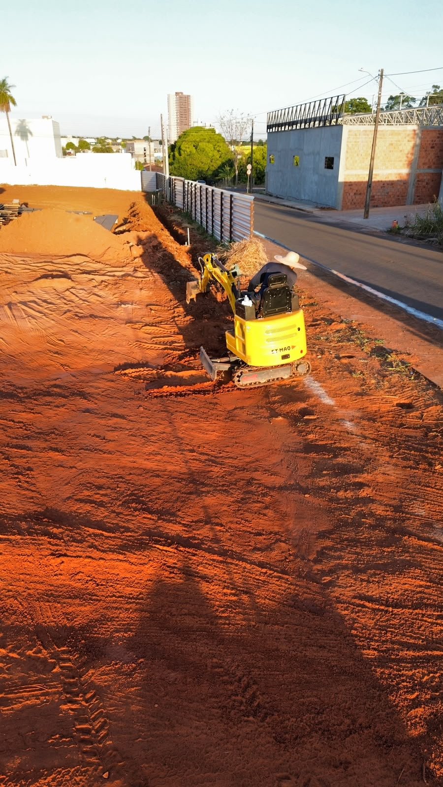 Mini escavadeira escavando vala rente ao alambrado da obra