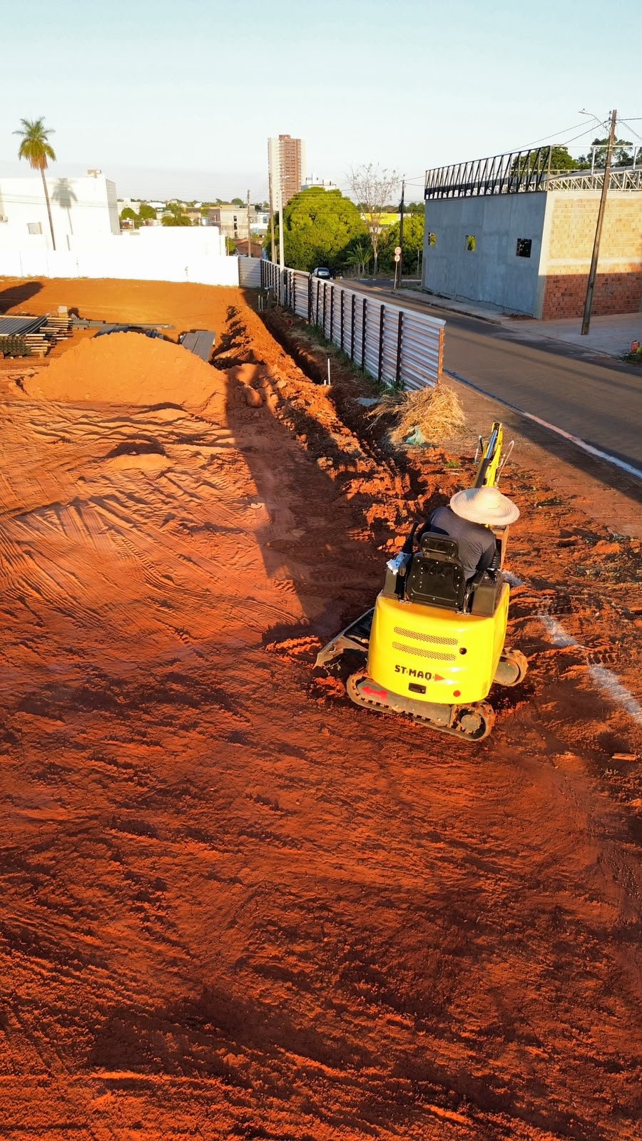 Terreno nivelado com vala aberta na lateral e mini escavadeira em operação